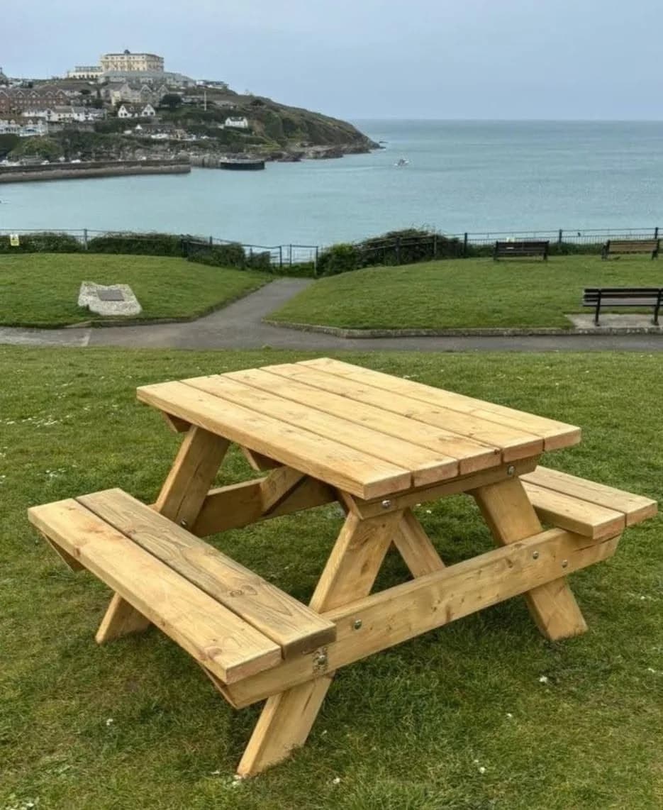 Substantial timber picnic table on grass overlooking the Cornish coast